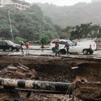 Severe flood damage to a road in South Africa with collapsed infrastructure, exposed pipes, stranded vehicles, and pedestrians during heavy rainfall, illustrating the growing impact of extreme weather on property and infrastructure.