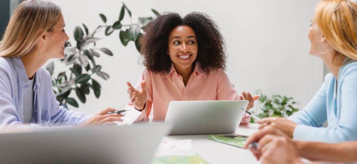 Employees discussing healthcare benefit options around a table with a laptop during a workplace meeting.